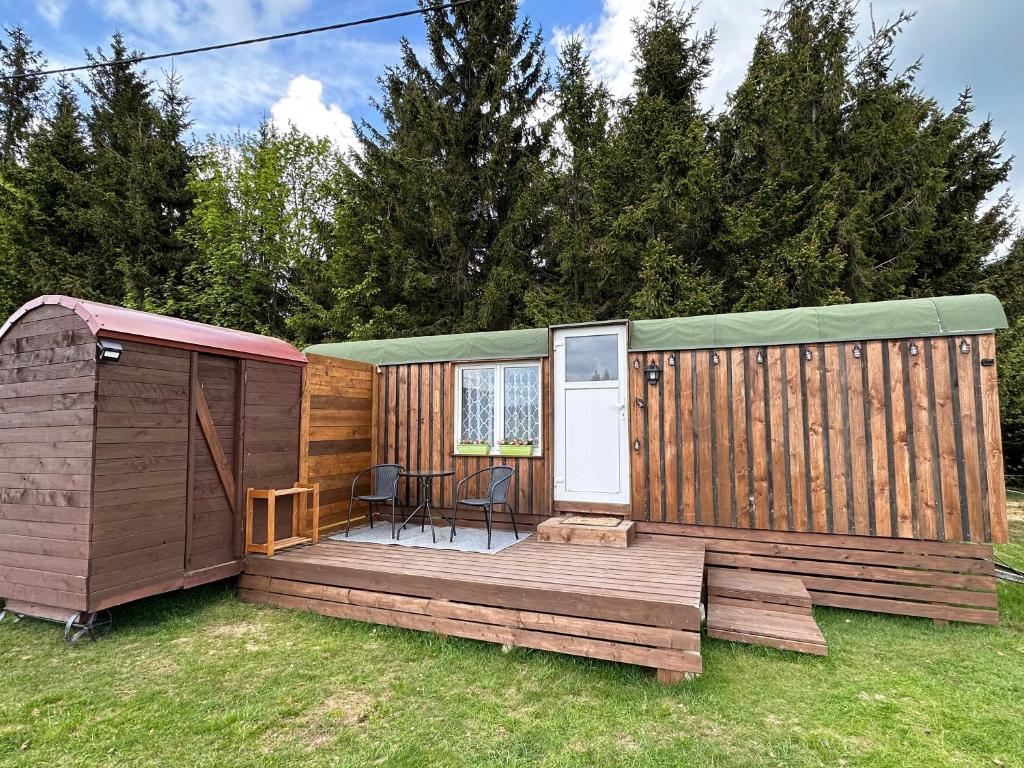 a large wooden cabin with a deck in the grass at Horská maringotka na farmě in Klíny