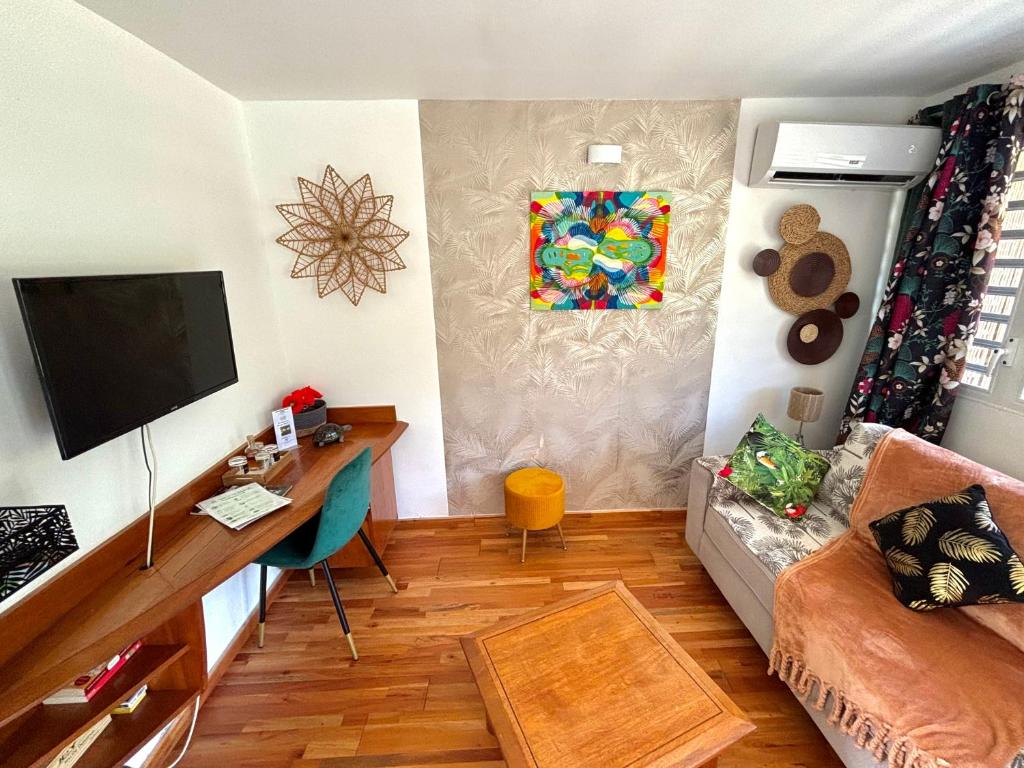 a living room with a tv and a couch and a desk at Bungalow La Kawannaise - Piscine, Terrasse, Plage in Grand-Bourg