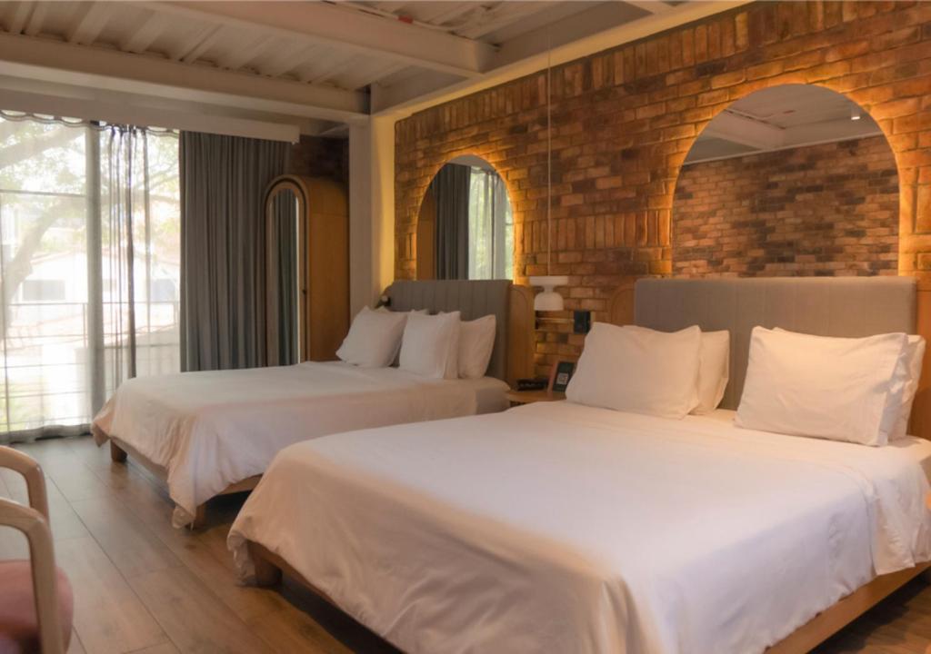 2 Betten in einem Hotelzimmer mit weißer Bettwäsche in der Unterkunft Nomada Hotel Origen in Medellín