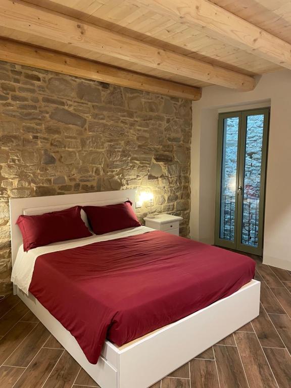 una camera con letto rosso e parete in pietra di Albergo del Bramante a Roccaverano