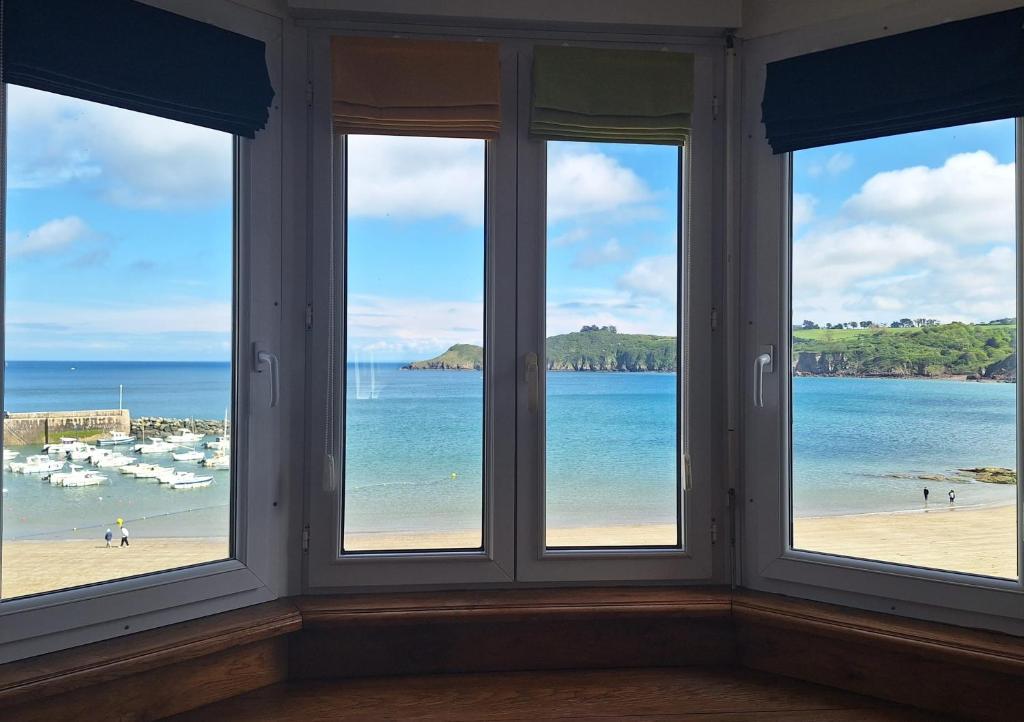 a room with three windows looking out at a beach at Face a la mer avec terrasse ensoleillee Brehec in Plouha