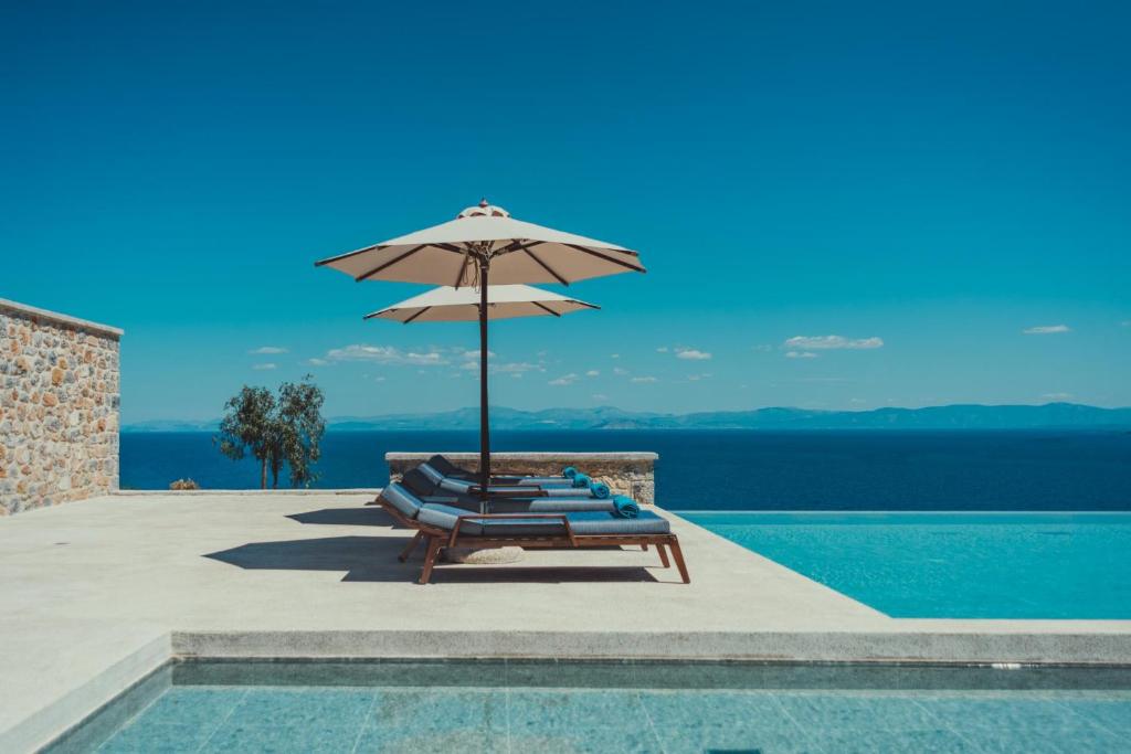 un grupo de tumbonas con sombrilla junto a la piscina en Sampatiki Suites - 4 Star Seaview Luxury Suites With Breakfast And Spa - Opened 2024, en Leonidio