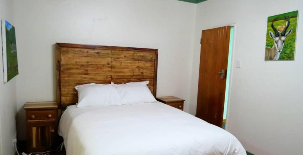Schlafzimmer mit einem weißen Bett und einem Kopfteil aus Holz in der Unterkunft Vimbainashe Villas 