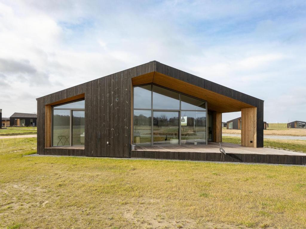 een houten huis met grote ramen in een veld bij Charming holiday home with garden in Wissenkerke