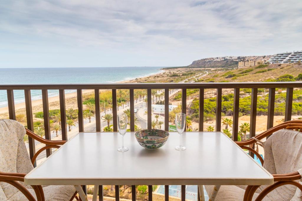 a table with two wine glasses on a balcony with the beach at AP Over the Sea in Arenales del Sol