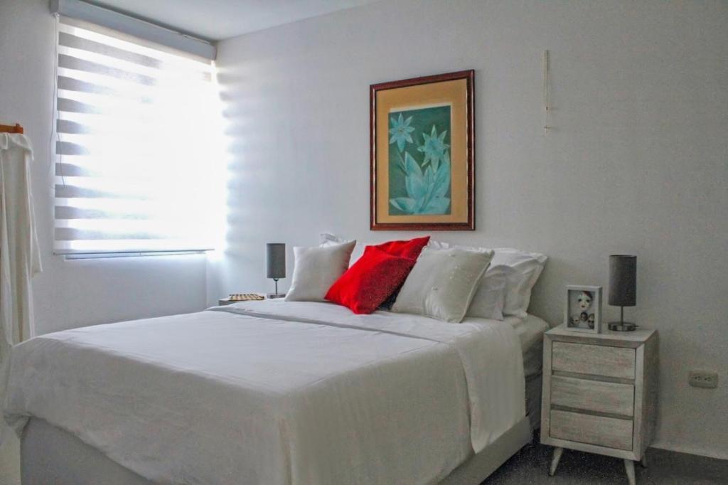 Dormitorio blanco con cama blanca y almohadas rojas en Apartamento de Yuly, en Santa Marta