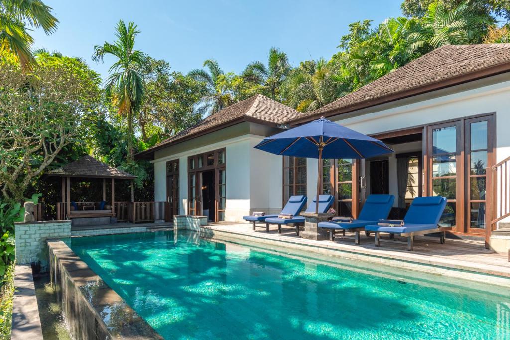 a villa with a swimming pool with chairs and an umbrella at Villa Umah Raja in Lovina