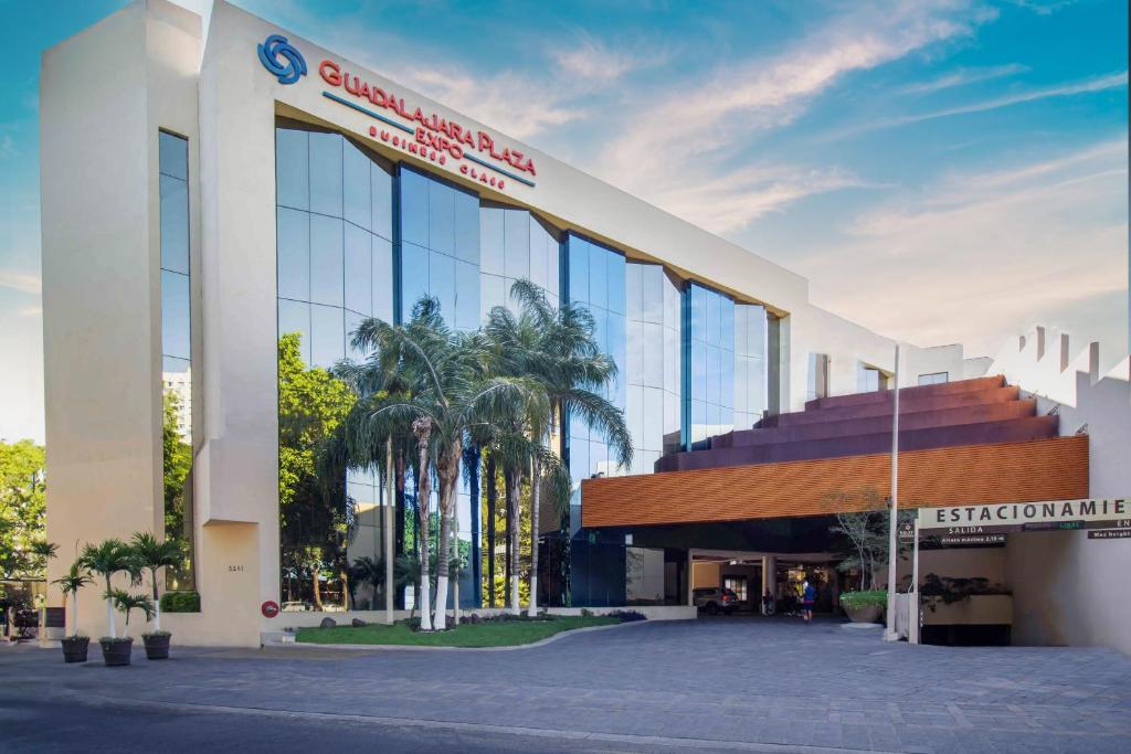 a large building with glass windows and palm trees at Hotel Guadalajara Plaza Expo in Guadalajara