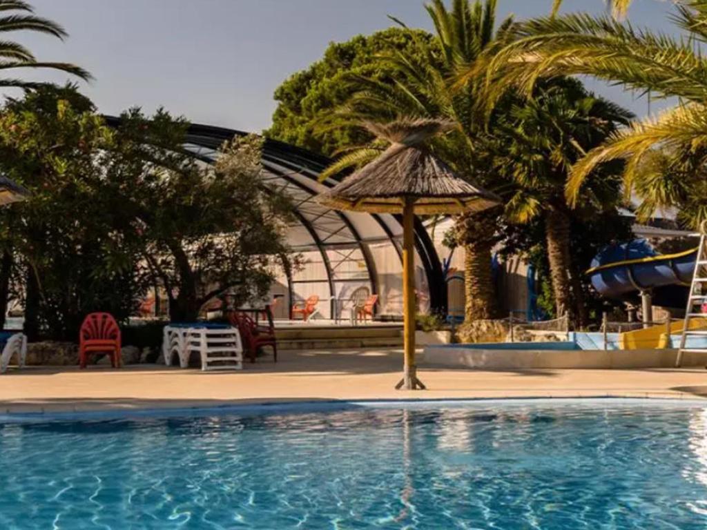 - une piscine entourée d'un parasol et de palmiers dans l'établissement Chalet de Luxe au Calme avec Piscines Chauffées, Clim et Prestations Haut de Gamme - FR-1-778-24, à Saint-Georges-dʼOléron