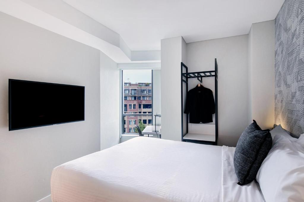a white bedroom with a bed and a tv at Kith Hotel Darling Harbour in Sydney