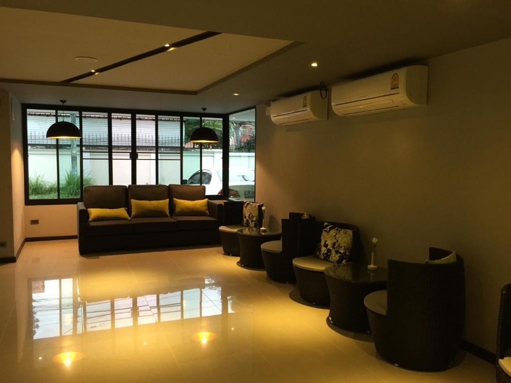 A spacious lounge with a sofa, individual chairs, pendant lights and large windows.