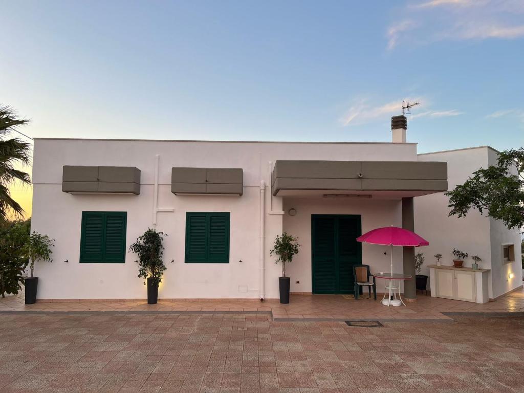 Um edifício branco com um guarda-chuva cor-de-rosa à frente. em Fusella Country House/Villa a Polignano Vista Mare em Polignano a Mare