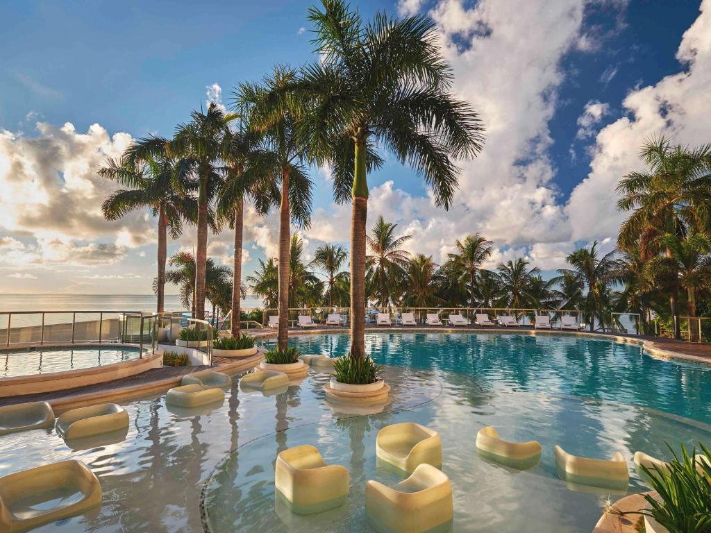 a large swimming pool with chairs and palm trees at Mövenpick Hotel Mactan Island Cebu in Mactan