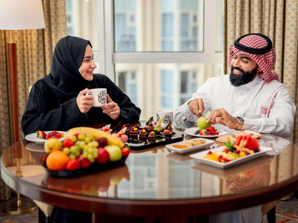 a man and woman sitting at a table with food at Swissotel Al Maqam Makkah in Mecca