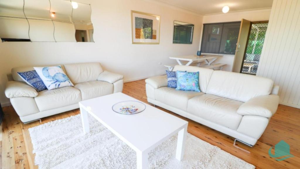 a living room with two white couches and a table at Coastal Horizons Beach House in Caves Beach