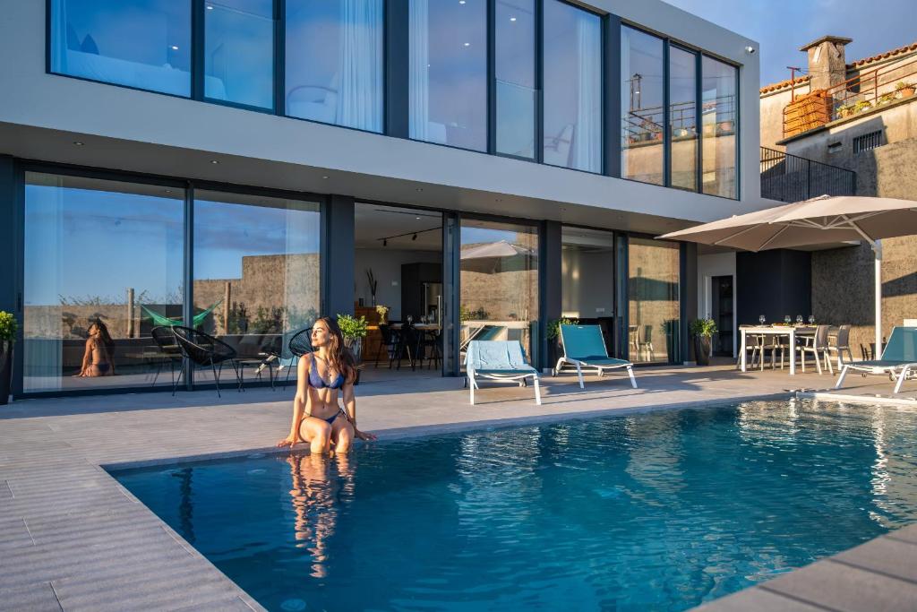 Eine Frau, die in einem Pool neben einem Haus sitzt. in der Unterkunft Villa Elysian Oasis by Homie in Prazeres