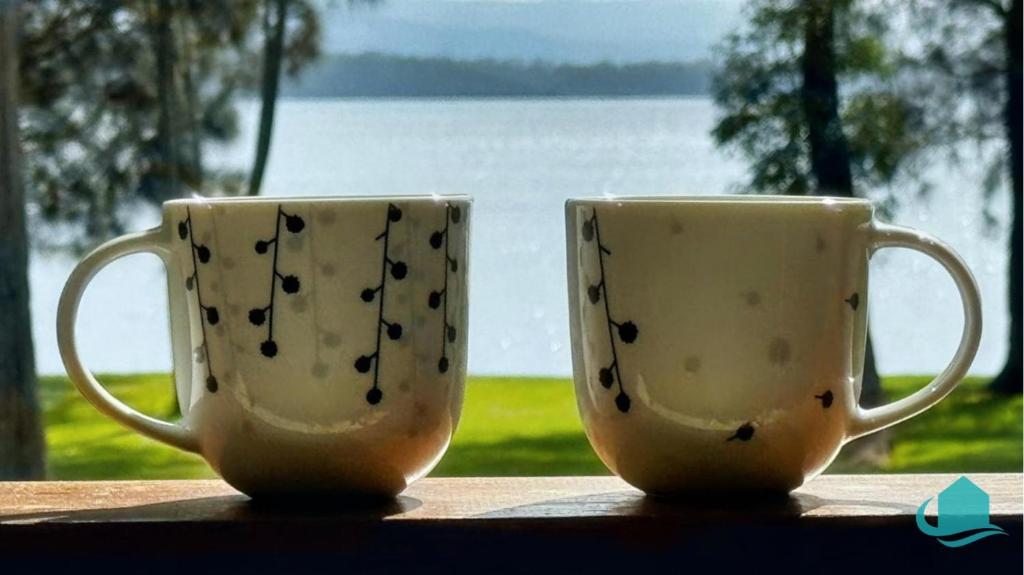 dos tazas de café sentadas en una mesa frente a una ventana en Casuarina Waters - waterfront home on Lake Macquarie, en Bonnells Bay