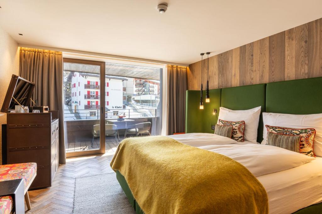 a bedroom with a large bed with a green headboard at Hotel ZERMAMA Zermatt in Zermatt