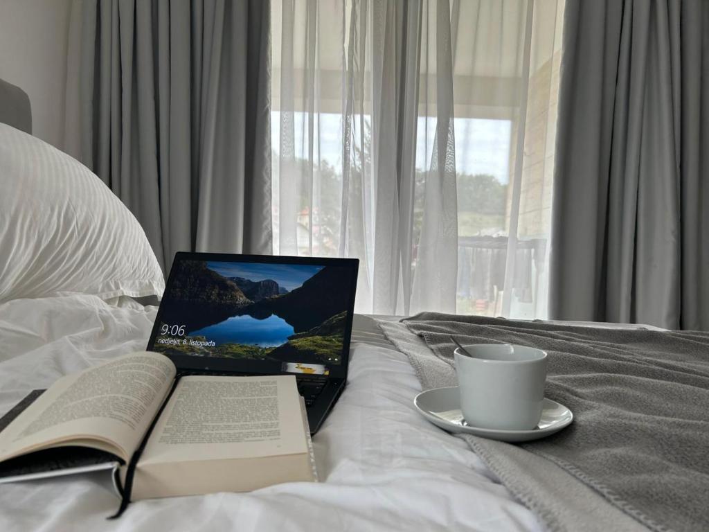 a laptop on a bed with a book and a cup of coffee at CASA V BENCUN Deluxe Queen Rooms in Kiseljak