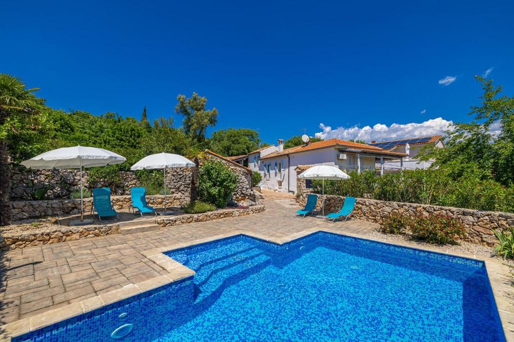 a swimming pool in a yard with blue chairs and umbrellas at Villa Neva - Cizici, Krk in Čižići