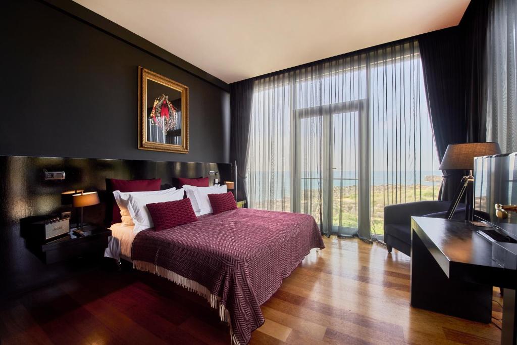 a bedroom with a bed and a desk and a large window at Farol Hotel in Cascais