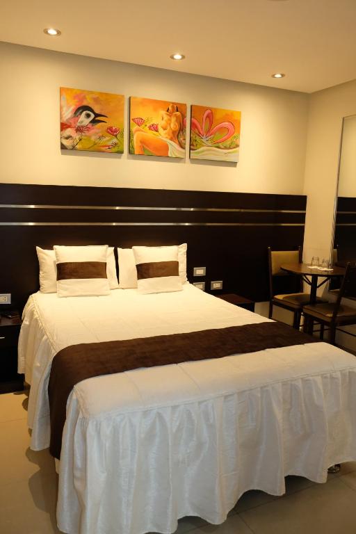a bedroom with a large bed and some paintings on the wall at Hotel Puma'r Tacna in Tacna