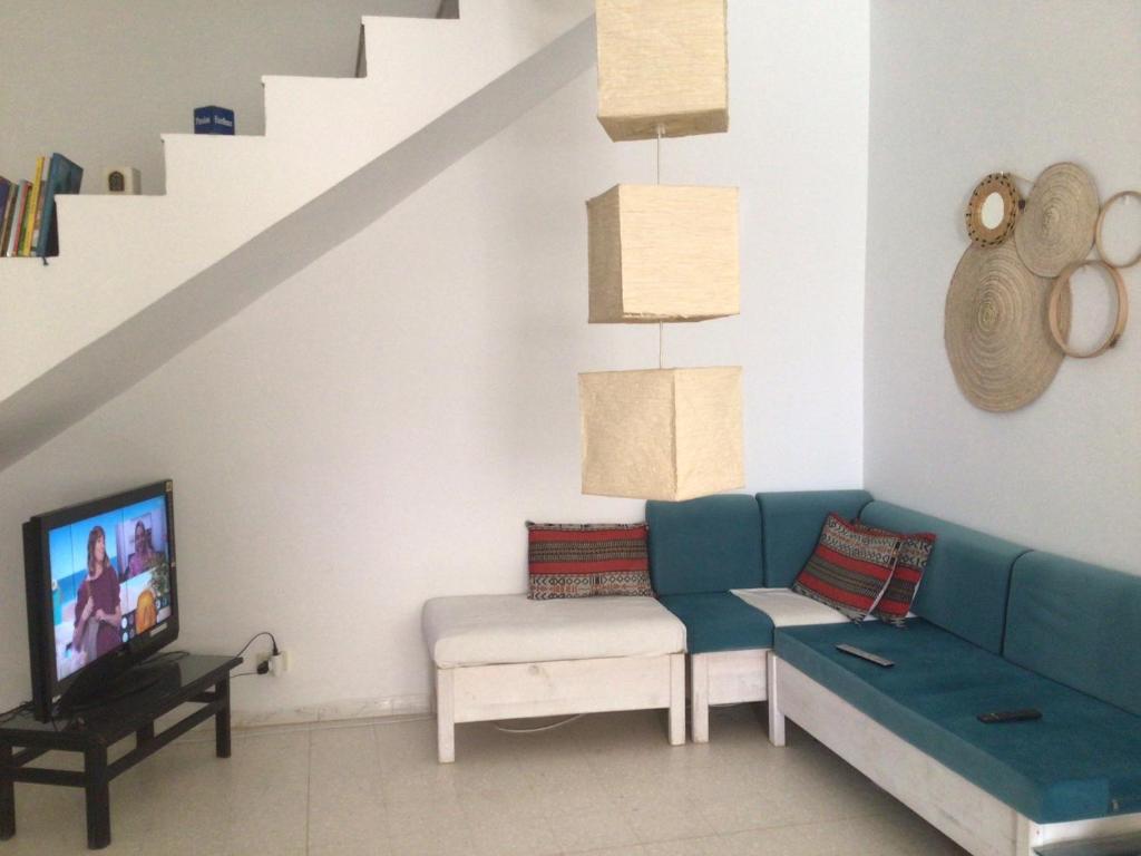 ein Wohnzimmer mit einem blauen Sofa und einem Fernseher in der Unterkunft Jolie petite maison à Djerba Houmt Souk in Al Ḩārah al Kabīrah