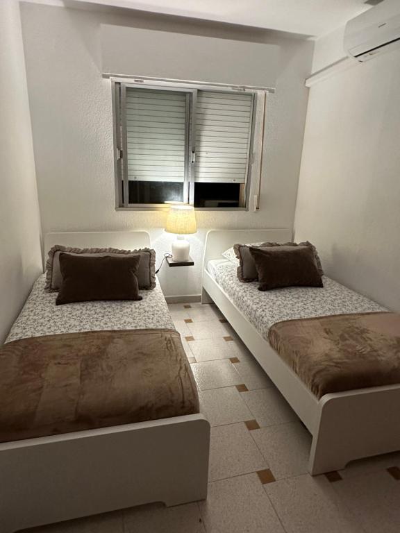 two beds in a white room with a window at Maison Lo pagan San Pedro del pinatar murcia in San Pedro del Pinatar