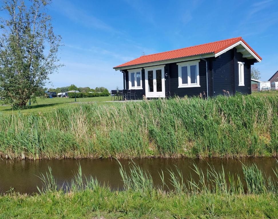 Vakantiehuisje vlakbij Leeuwarden, Swichumer Pleats في Swichum: منزل أسود بسقف احمر بجوار نهر