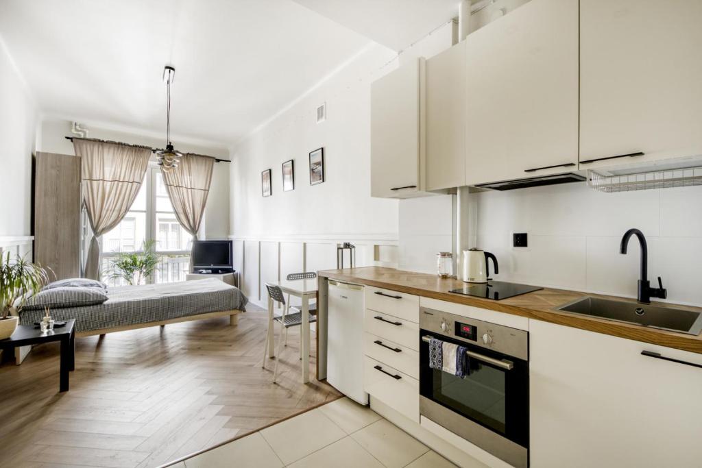 a kitchen with white cabinets and a living room with a bed at Studio Marszałkowska in Warsaw