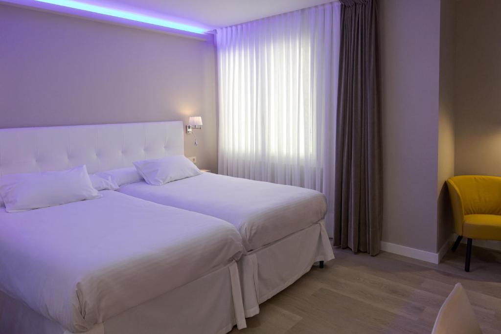 a bedroom with a large white bed and a yellow chair at Hotel Jucamar in Cangas de Morrazo