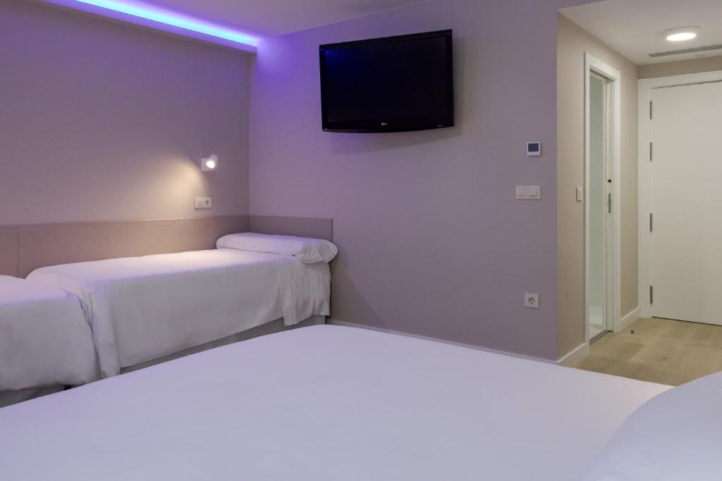a room with two beds and a tv on the wall at Hotel Jucamar in Cangas de Morrazo