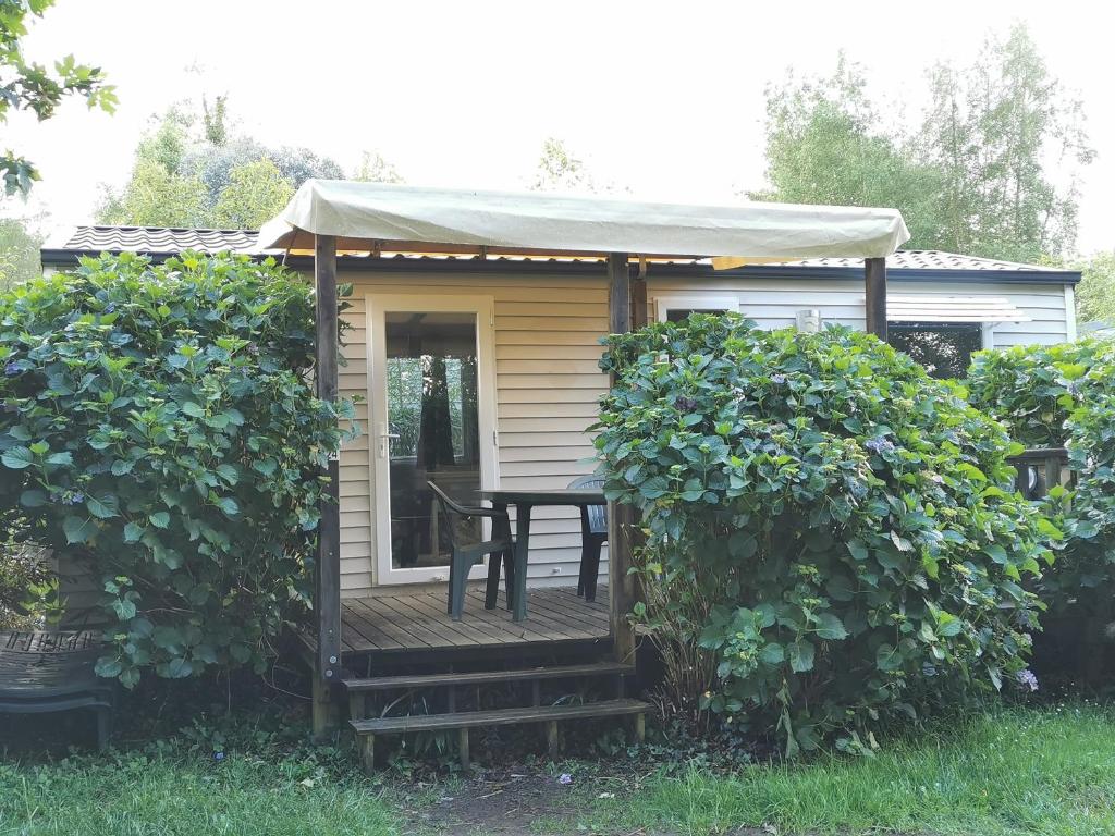Cette petite maison dispose d'une terrasse couverte avec une table. dans l'établissement Mobil-home dans le calme du Domaine de Lanniron R24, à Quimper