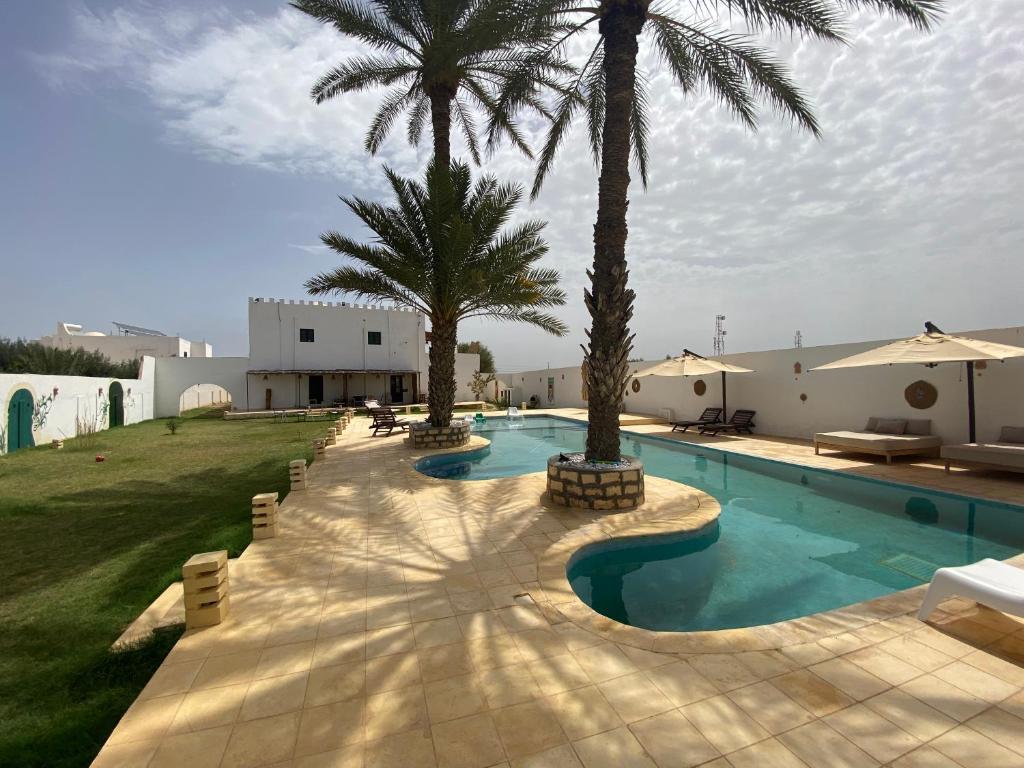 een zwembad met twee palmbomen naast een gebouw bij Dar Oueghlani - Maison d'hôtes in El Mây