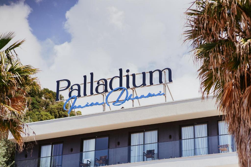 a sign on top of a building with palm trees at Palladium Beach Hotel in Dhërmi