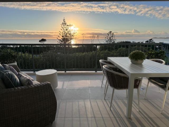 a patio with a table and chairs and the sunset at Panoramic Ocean View 2 bed 2 bath in Alexandra Headland
