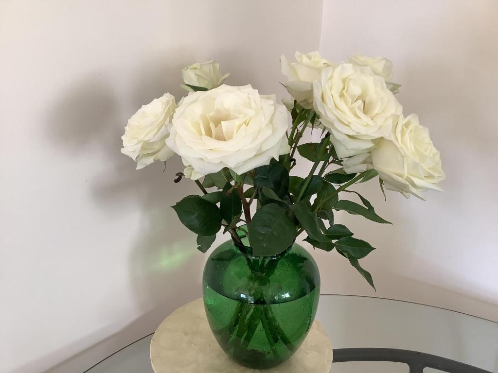 a green vase filled with white roses on a table at Maggie's Nest-Come & Rest in Killarney Vale