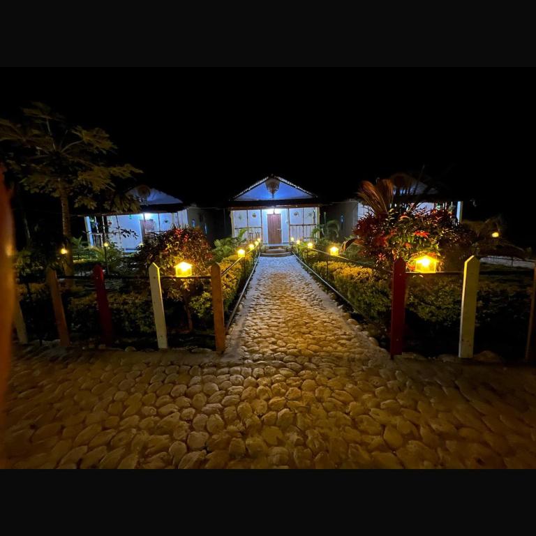 a pathway leading to a building at night with lights at Falcon Jungle Resort in Jyoti Gaon