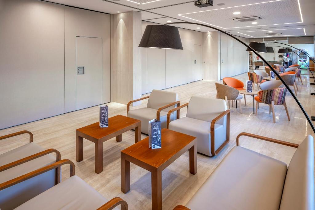 una sala de espera con sillas y mesas blancas en GHT Oasis Tossa & Spa, en Tossa de Mar