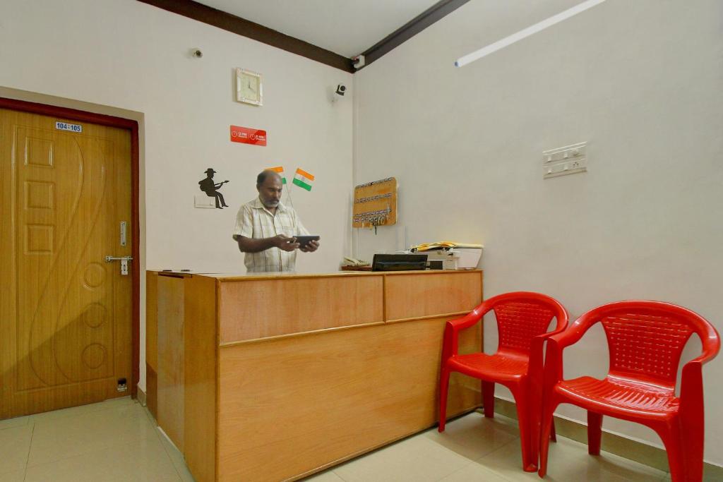 a man standing at a counter with two red chairs at OYO Flagship Ananda Inn in Madurai