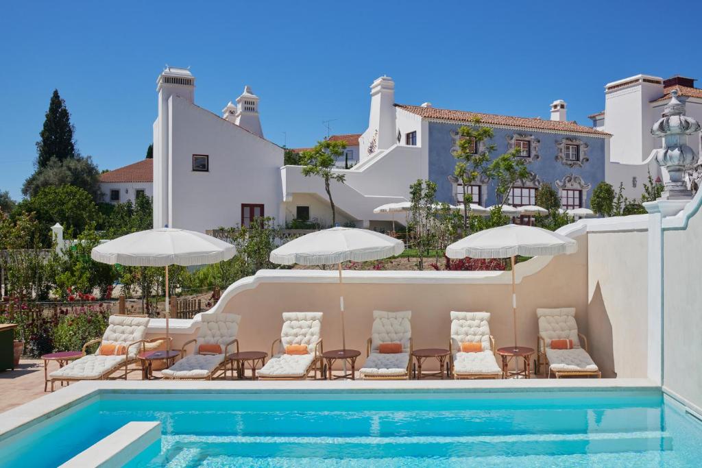 a pool with chairs and umbrellas next to a building at Vermelho Melides - Relais & Châteaux in Melides