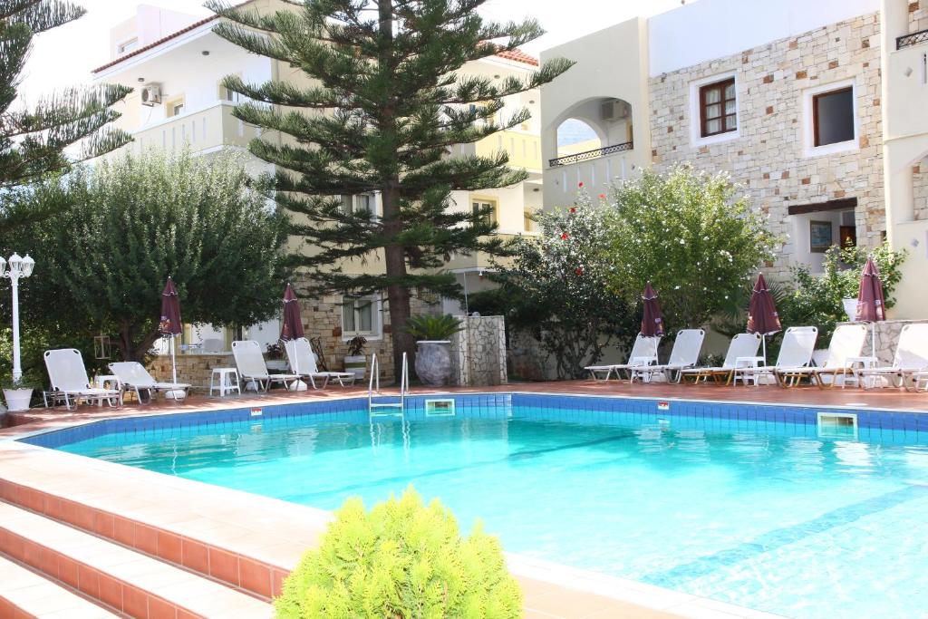 a swimming pool in a hotel with chairs and a tree at Nikos Apartments in Stalís