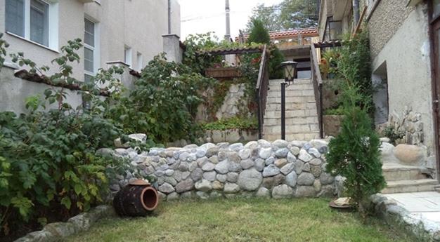 a stone wall in a yard next to a building at Къща за гости Сара in Velingrad
