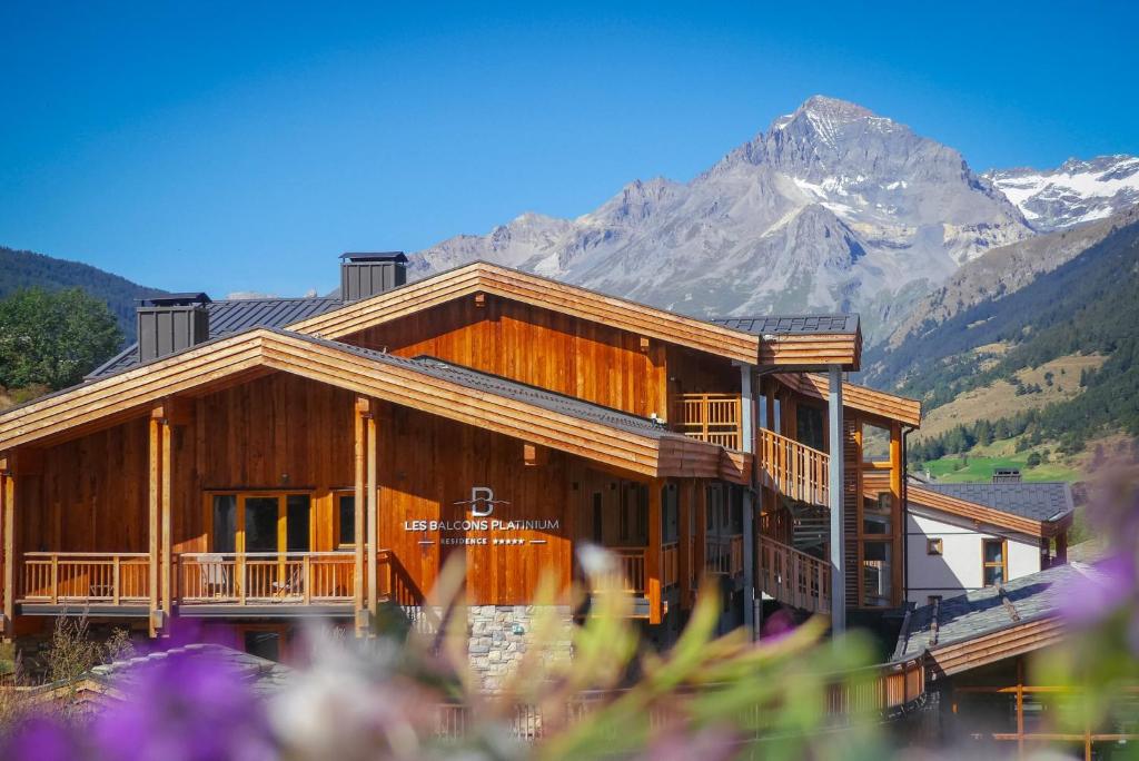 a large wooden house with mountains in the background at Les Balcons Platinium Val Cenis in Lanslevillard
