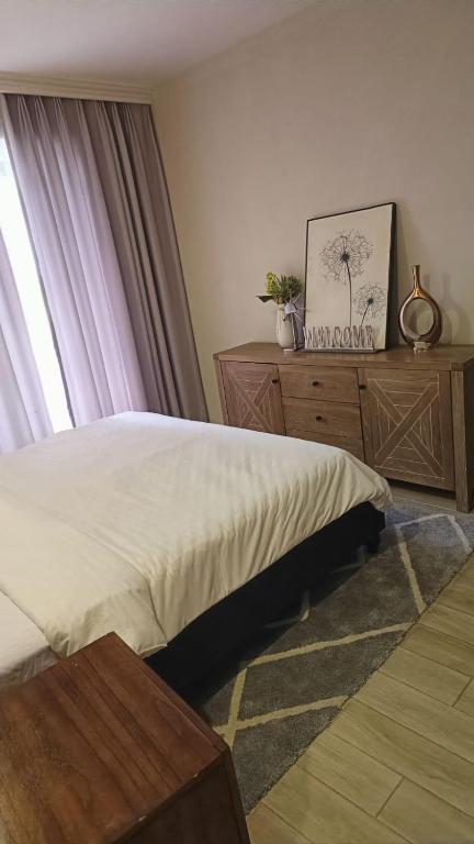 a bedroom with a bed and a dresser and a window at InDesign Makumbi Park Apartments near 67 airport hotel in Syokimau