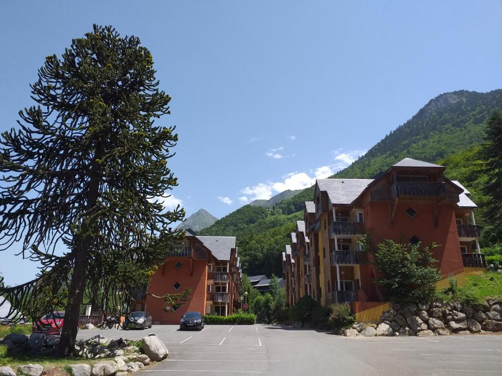 un aparcamiento con edificios y un árbol y montañas en Appartement F2 au domaine des 100 lacs - piscine - sauna - hammam en Cauterets