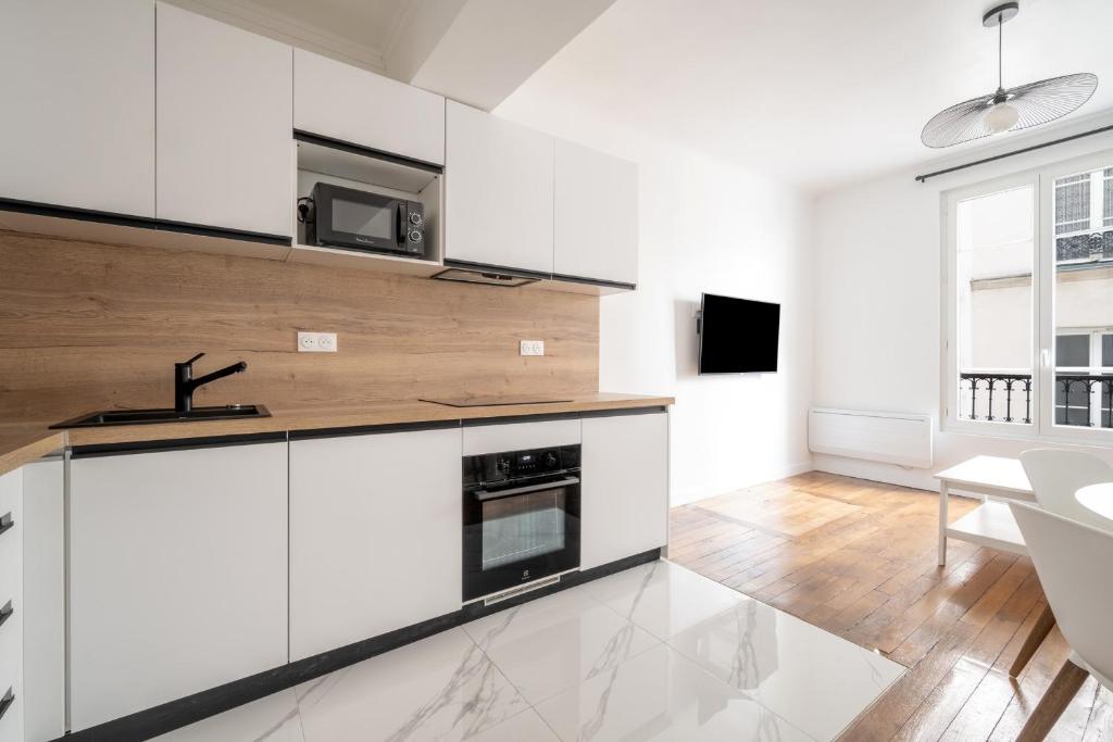 une cuisine avec des armoires blanches, un évier et un micro-ondes dans l'établissement Appartement Paris Blanche - Welkeys, à Paris