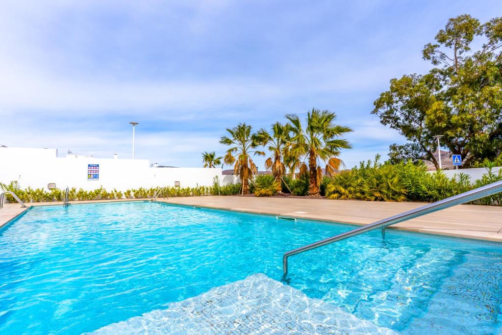 einen Pool mit blauem Wasser und Palmen in der Unterkunft San José Suites 3 Hab, Piscina, solárium y WiFi in Almería