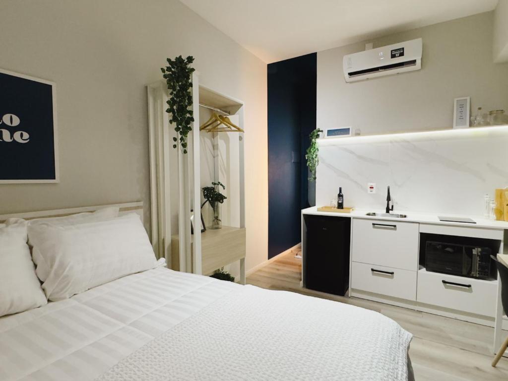 a bedroom with a white bed and a kitchen at Apê Metrô Higienópolis Mackenzie in Sao Paulo