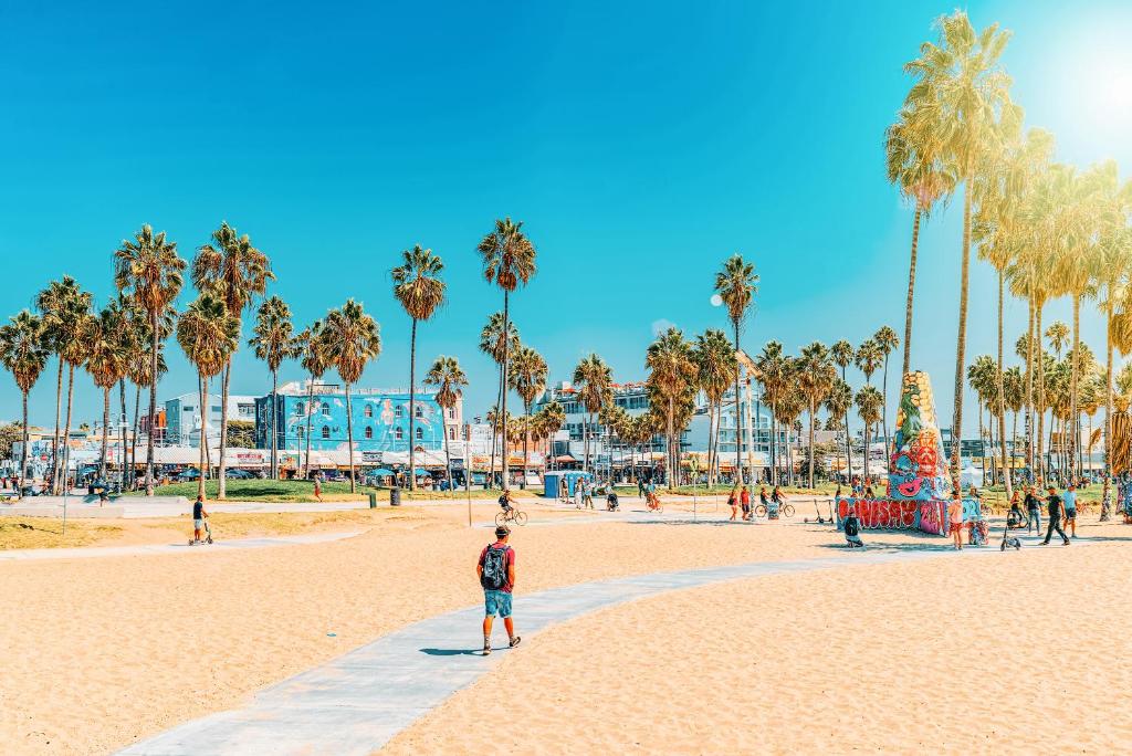 un uomo in piedi su una spiaggia con palme di Samesun Venice Beach Hotel & Hostel a Los Angeles